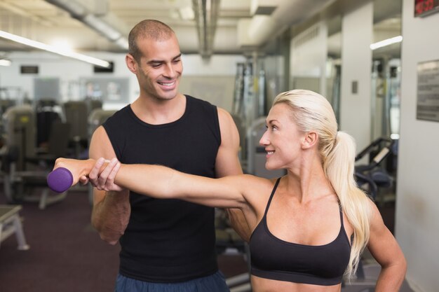 Formateur aidant une femme avec haltère dans une salle de sport