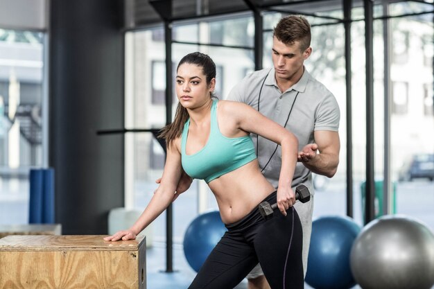 Formateur aidant une femme soulevant des haltères au gymnase