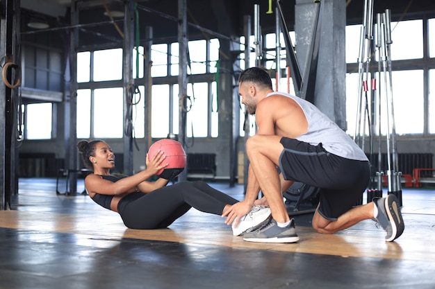 Formateur aidant une jeune femme à faire des exercices abdominaux dans une salle de sport.