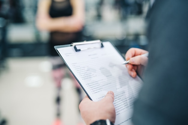 Formateur et client discutant de ses progrès au gymnase. Instructeur de gymnastique écrit sur le presse-papiers