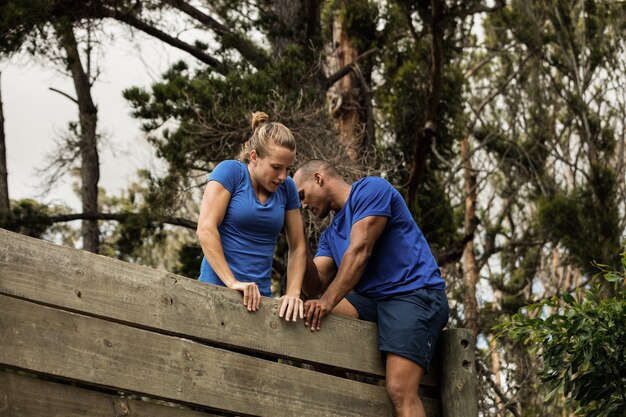 Formateur masculin aidant la femme à escalader un mur en bois