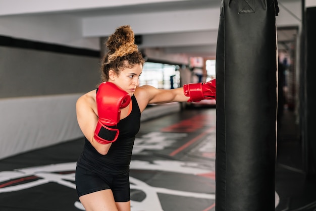 Formation de boxeur femme avec des gants de boxe rouges poinçonnage directement dans un sac de boxe dans une salle de sport