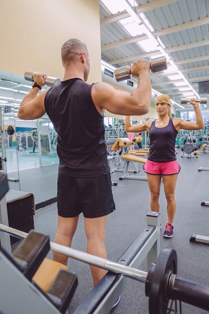 Formation d'entraîneur d'homme à une belle femme avec des exercices d'haltères sur un centre de remise en forme. Concept d'entraîneur personnel.