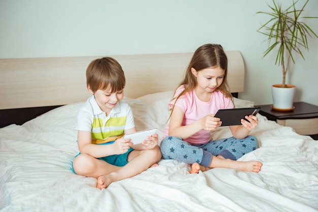 Formation en ligne à distance. Enfants assis avec une tablette sur le lit dans la chambre