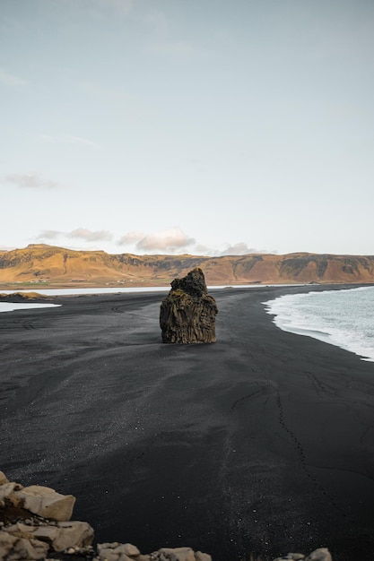 Photo formation rocheuse isolée au milieu d'une plage de sable noir en islande avec la mer à côté