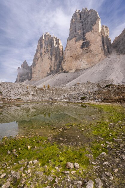 Photo formation rocheuse massive de tre cime reflétant dans un petit étang des dolomites tirées verticalement en italie