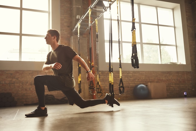 Formation TRX. Jeune homme athlétique dans les jambes d'entraînement de vêtements de sport avec des sangles de fitness trx dans la salle de sport