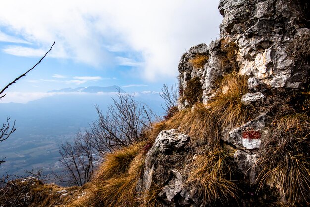 Photo formations rocheuses et sentiers entre des rochers et des arbres nus avec une vue sur la vallée d'astique et les nuages de sumano et le ciel bleu dans les alpes de vicenza vénétie italie