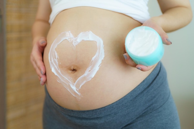 La forme blanche du cœur créée à partir de crème sur un gros ventre nu Prendre soin d'une peau parfaite et lisse