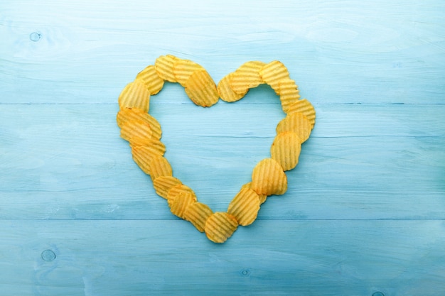 Forme de coeur de chips de pommes de terre sur un fond en bois bleu. Croustilles salées ondulées jaunes comme arrière-plan alimentaire.