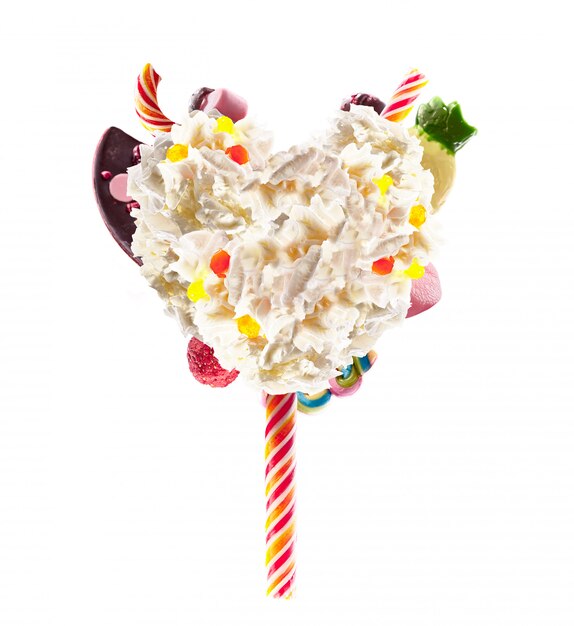 Forme de coeur de crème fouettée avec des bonbons, des gelées, vue de face du coeur. Tendance alimentaire fou freakshake. coeur de crème, plein de bonbons aux baies et à la gelée, concept de bonbons au chocolat isolé sur blanc.