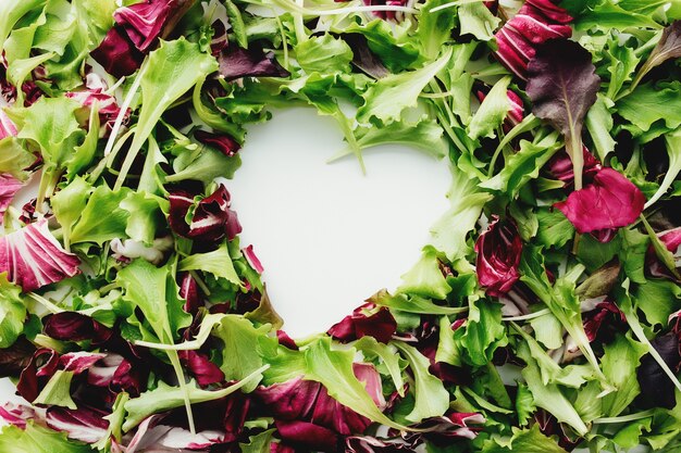 Forme de coeur de feuilles de salade vertes et violettes mélangent l'arrière-plan. Table blanche