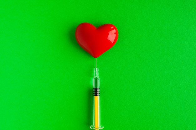 Forme de coeur volumétrique avec une seringue sur fond vert. À utiliser pour les problèmes cardiaques ou les concepts de maladie.