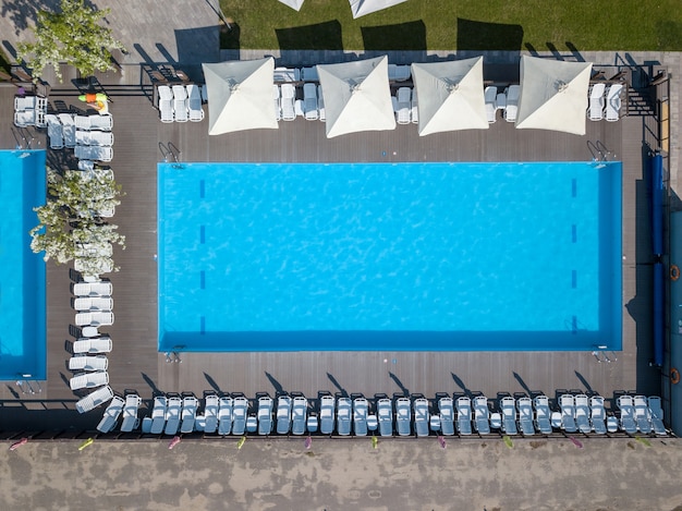 Forme et courbes de la grande piscine bleue avec lits et parasols sur le jardin verdoyant. Concept de vacances. Photo du drone