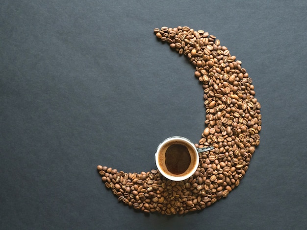 Forme de croissant faite de grains de café et d'une tasse de café noir. Vue de dessus.