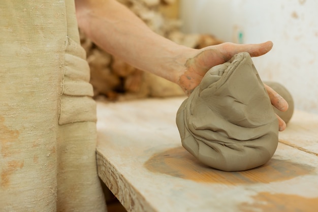 Photo former la figure de base. maître potier expérimenté tenant en place une nouvelle argile tout en commençant la journée dans un atelier de poterie