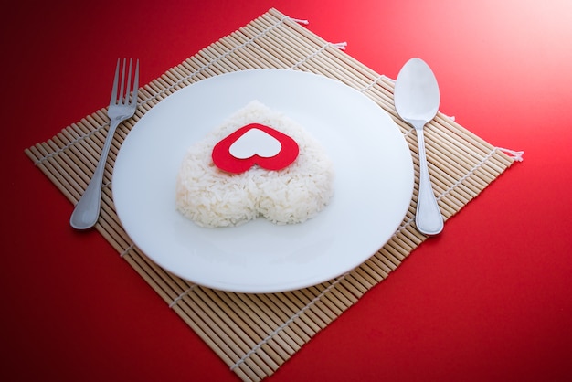 formes de coeur de riz cuit avec une cuillère et une fourchette sur plat blanc en Platemat et sur fond rouge