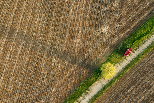 Formes géométriques abstraites de sol agricole sans semis, séparées en diagonale par la route et la voiture rouge dessus, dans les couleurs vertes et noires. Une vue plongeante depuis le drone.