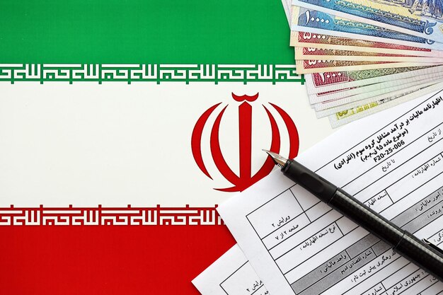 Photo formulaire de déclaration d'impôt sur le revenu annuel iranien f prêt à remplir sur la table avec un stylo et de l'argent iranien sur le drapeau