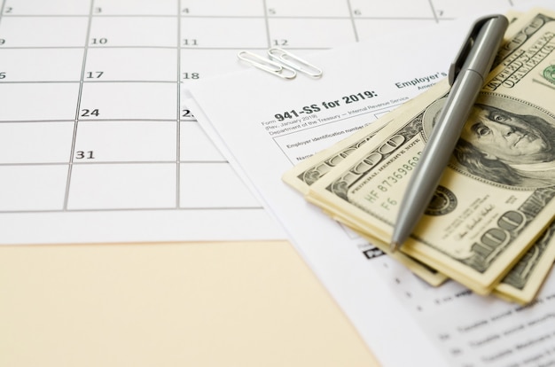 Formulaire IRS 941-SS La déclaration de revenus fédérale trimestrielle de l'employeur est vide avec un stylo et plusieurs centaines de dollars sur la page du calendrier
