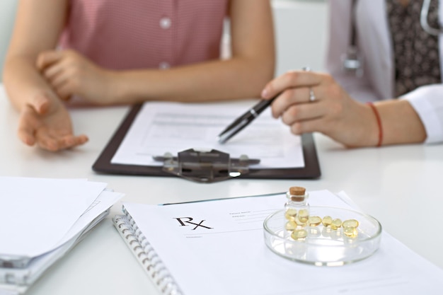 Le formulaire de prescription médicale, les gélules et les pilules se trouvent dans le contexte d'un médecin et d'un patient discutant des résultats de l'examen de santé.