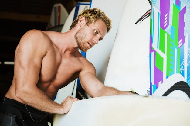 Photo fort beau jeune homme surfeur à la plage dans un garage avec surf.