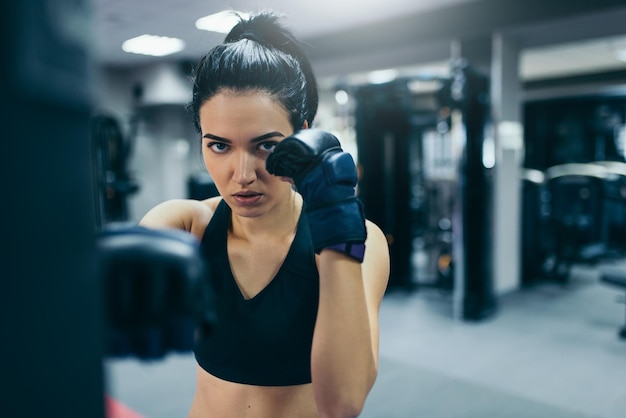 Forte séduisante femme athlète brune frappant un sac avec des gants de kickboxing noirs dans l'entraînement de gym Sport fitness style de vie et concept de personnes