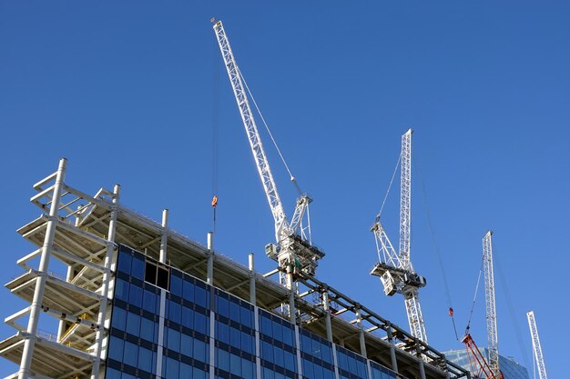 Photo de fortes grues de tour de levage sur la section supérieure étant la construction d'un gratte-ciel haut moderne