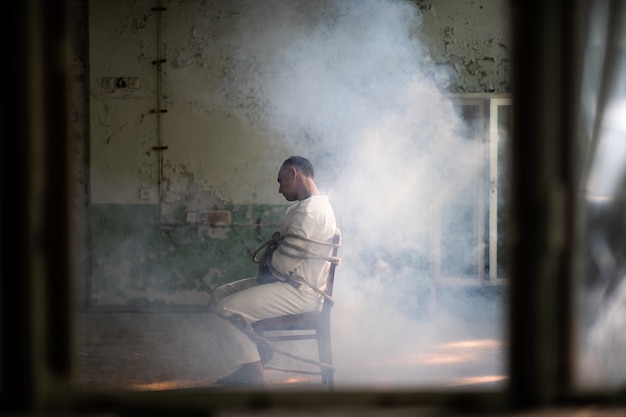 Un Fou En Camisole De Force Est Attaché à Une Chaise Dans Une Vieille Clinique Abandonnée.