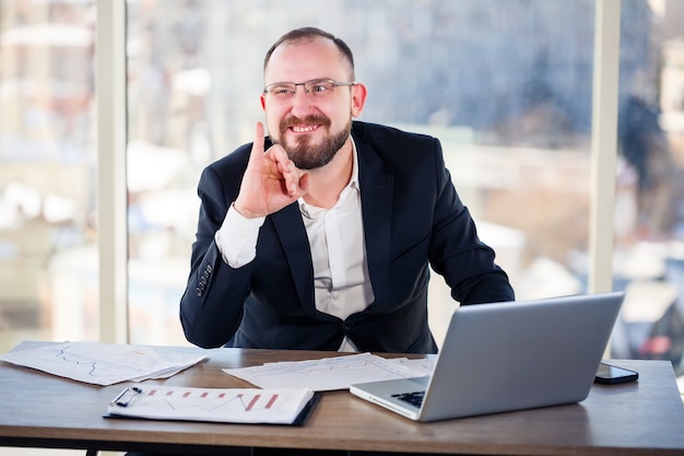 Le fou d'entreprise est assis devant l'ordinateur au bureau et devient fou, le portrait émotionnel de l'homme à la table. Travailleur fou sur son lieu de travail