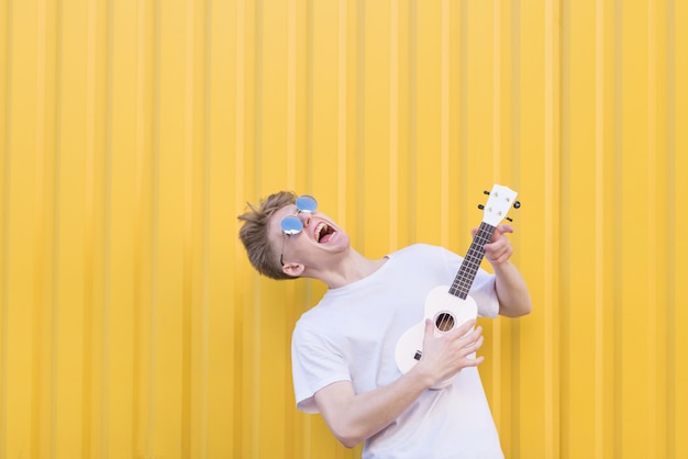 Fou Jeune Homme Joue Du Ukulélé Sur Un Mur Jaune. Musicien Expressif Jouant De La Guitare. Concept Musical