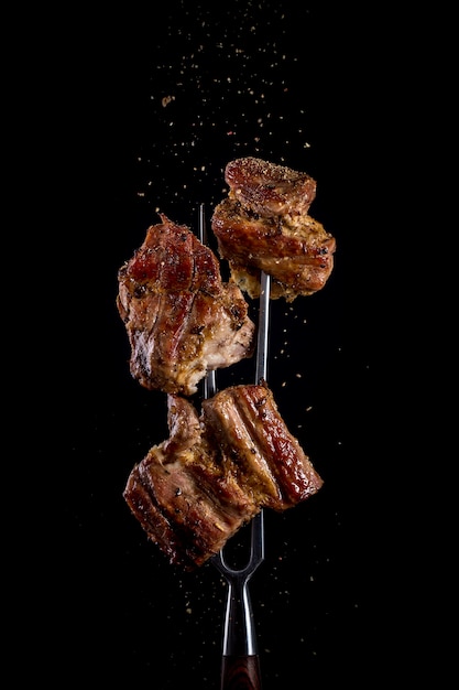Fourche avec des morceaux de viande délicieuse grillée sur noir