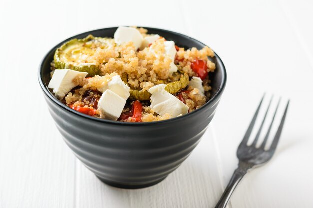 Une fourchette à côté d'un bol de salade de quinoa et légumes cuits au four sur un tableau blanc