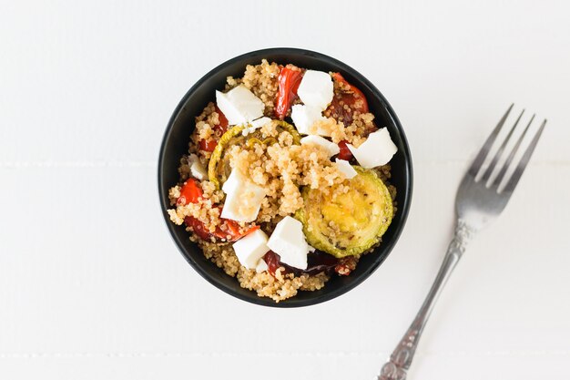 Une fourchette à côté d'une salade de légumes cuits au four, fromage et quinoa bouilli. Plat végétarien. La vue du haut. Mise à plat.