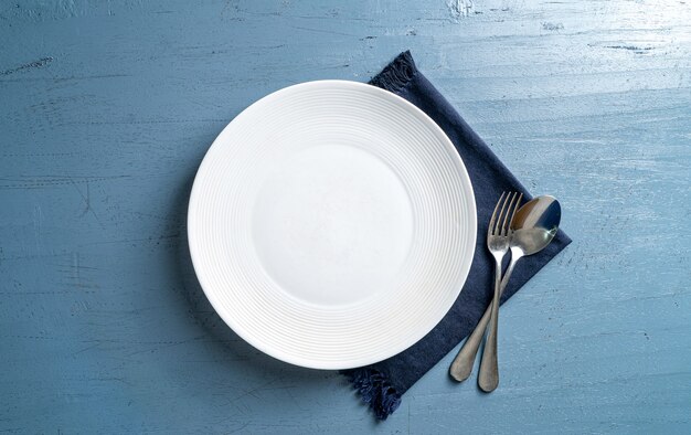 fourchette et cuillère à assiette blanche vide sur une table en bois bleu clair avec une nappe bleu foncé vue de dessus maquette