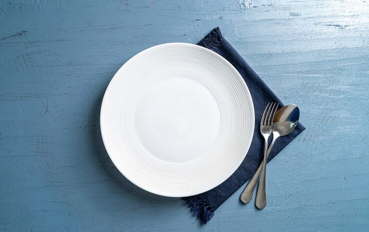 Photo fourchette et cuillère à assiette blanche vide sur une table en bois bleu clair avec une nappe bleu foncé vue de dessus maquette