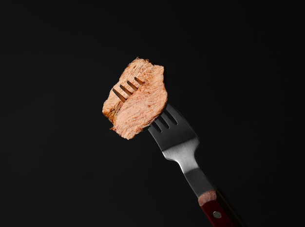 Photo fourchette avec morceau de steak savoureux sur fond noir vue rapprochée