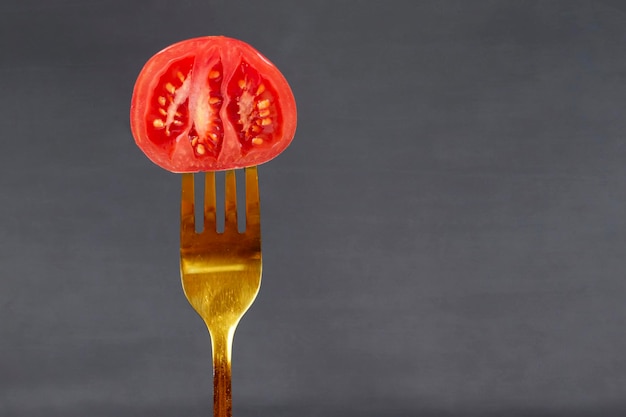 Sur une fourchette en or une tomate rouge sur fond gris Nourriture créative ou légumes Concept d'aliments sains