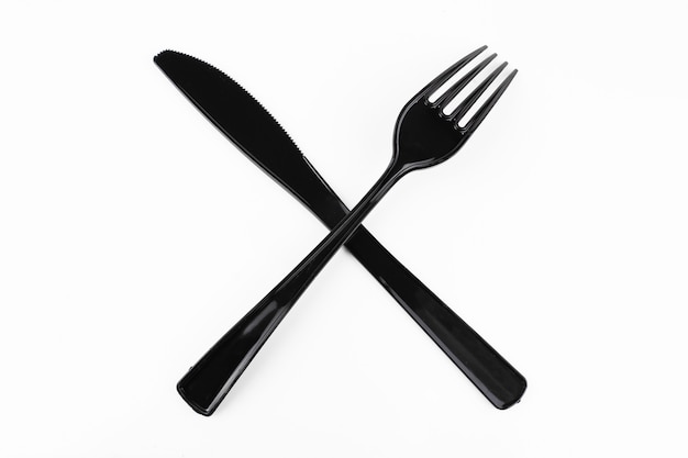 Fourchette de table noire et couteau croisés sur fond blanc.