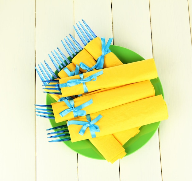 Des fourchettes en plastique bleu enveloppées dans des serviettes en papier jaune sur un fond en bois de couleur