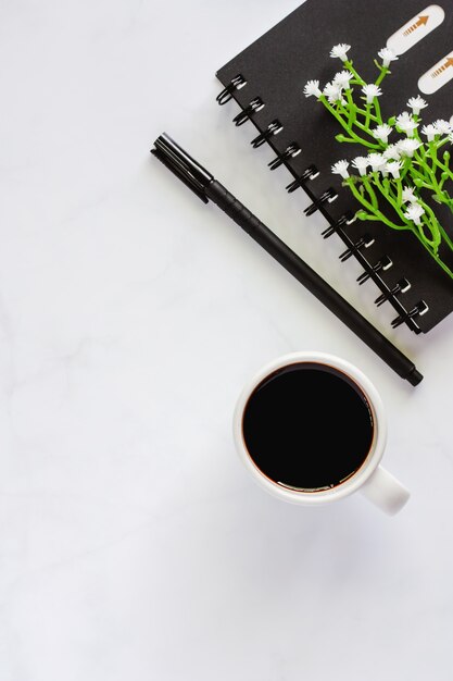 Fournitures de bureau avec cahier à spirale, stylo, tasse de café noir et petite plante artificielle