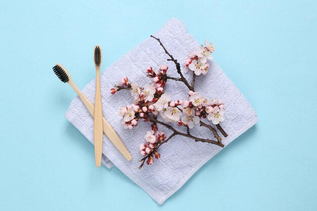 Fournitures d'hygiène pour les soins personnels avec de belles branches fleuries Brosses à dents écologiques et serviette sur fond bleu