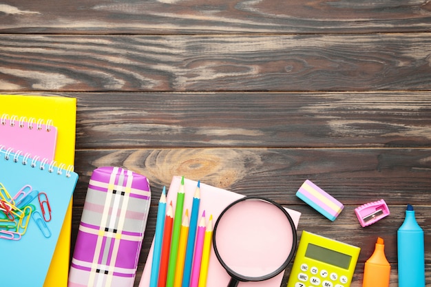 Fournitures scolaires, accessoires de papeterie avec espace copie sur fond en bois marron. Mise à plat, vue de dessus