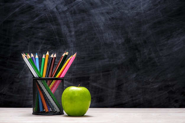 Fournitures scolaires et de bureau et pomme devant le tableau noir.