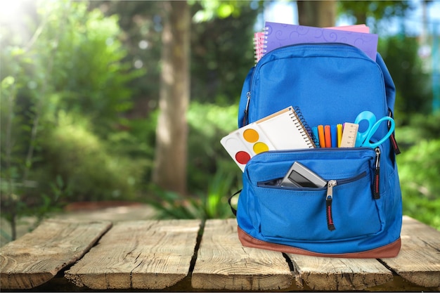 Fournitures scolaires colorées en sac à dos sur fond de bois