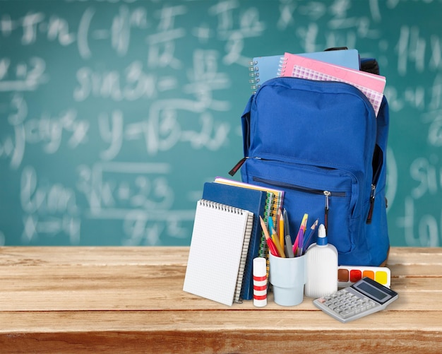 Fournitures scolaires colorées en sac à dos sur fond de tableau noir