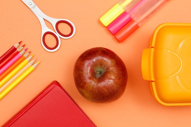 Fournitures scolaires. Crayons de couleur, livre, pomme, ciseaux, feutres et boîte à lunch sur fond rose. Vue de dessus. Retour au concept de l'école. Couleurs pastel