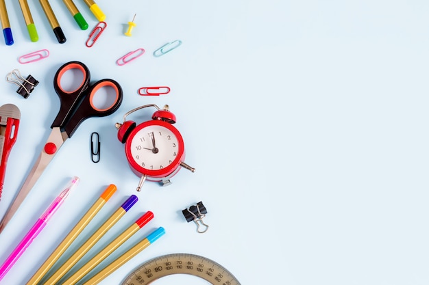 Fournitures scolaires sur un fond bleu avec fond pour la conception. Crayons, ciseaux, cahier, réveil, vue de dessus. Retour à l'école