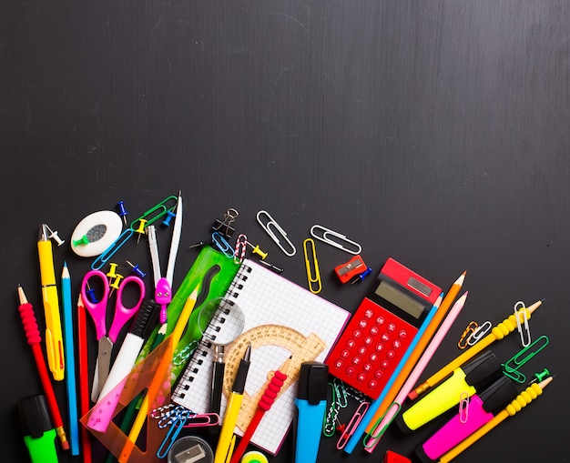 Fournitures scolaires sur fond noir. Disposition plate.