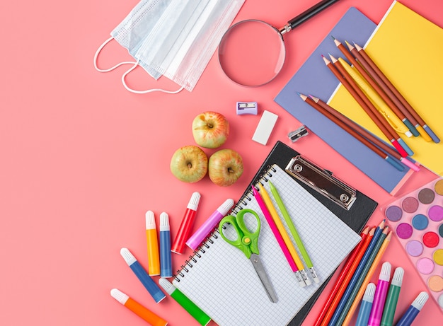 Fournitures scolaires et masques de protection sur fond rose, vue de dessus, espace de copie